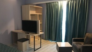 Una habitación moderna con televisión de pantalla plana sobre un mueble de madera, un sofá, una mesa de centro y un ventanal con cortinas estampadas.