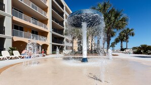 A water fountain with multiple jets, surrounded by a sandy area and white lounge chairs. - Azure 223 | 3BR Coastline View | FREE Beach Service (Fort Walton Beach)