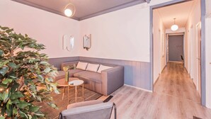 A modern living room with a grey sofa, a patterned rug, and a potted plant. - Sweett | Rocafort Principal 1 (Barcelona)