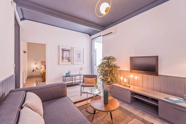 A modern living room with a sofa, a coffee table, and a TV. There is a plant and a lamp on the table.