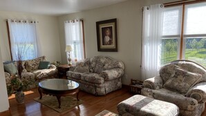 Una sala con sofás de estampado floral, una mesa de centro de vidrio y piso de madera.