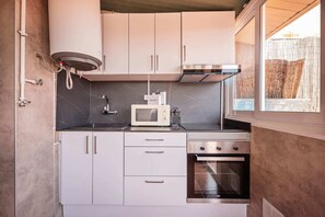 A compact kitchen with white cabinets, a microwave, a stove, and a window with a view of a bamboo fence. - Sweett | Rocafort Atic 1 (Barcelona)