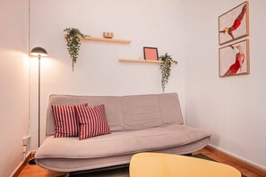 A modern living room with a sofa, a floor lamp, and wall-mounted shelves with plants and artwork. - Sweett | Rocafort Atic 1 (Barcelona)
