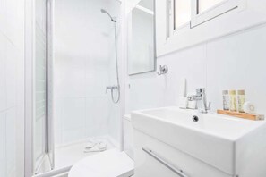 A modern bathroom with a glass shower enclosure, a white sink with toiletries, and a toilet.