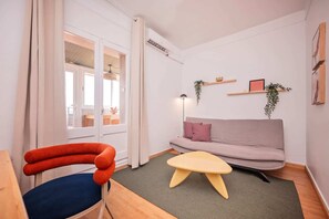 Een woonkamer met een bank, een stoel, een bijzettafeltje en uitzicht door een deur.
