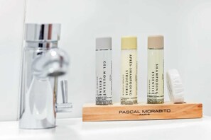 A bathroom with a modern faucet, a wooden soap dish, and three bottles of shampoo and conditioner.