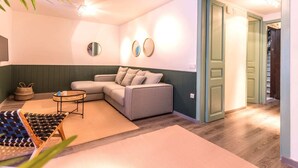 A cozy living room with a grey sofa, a small round coffee table, and a woven basket. There are two round mirrors on the wall and a door leading to another room. - Sweett | Rocafort Entresuelo 2 (Barcelona)