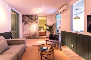 Un salon chaleureux avec un canapé, une petite table ronde, un fauteuil et une grande fenêtre donnant sur un beau paysage.