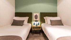 A hotel room with two single beds, a small table with a lamp, and a framed picture on the wall. - Sweett | Rocafort Entresuelo 2 (Barcelona)