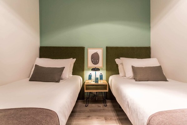 Une chambre d’hôtel avec deux lits simples, une petite table avec une lampe et un tableau encadré au mur.
