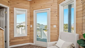 Una habitación con paneles de madera, una puerta blanca, vista a un balcón y un sofá color beige.