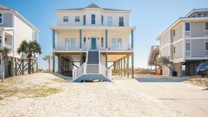 Una propiedad frente a la playa con una casa de dos pisos, que cuenta con un porche cubierto y una escalera que conduce al nivel superior.