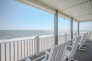 A beachside deck with white rocking chairs and a white railing overlooking the ocean.