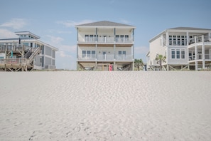 A beachfront property with multiple levels, balconies, and a sandy beach in the foreground.