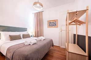 Una camera d'albergo con un letto, un lampadario, un appendiabiti in legno e una porta.
