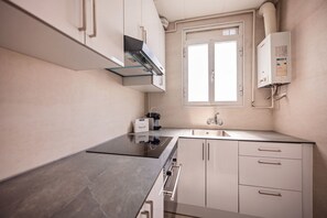 A modern kitchen with a built-in oven, a sink, and a window above the countertop. - Sweett | Rocafort 504 (Barcelona)