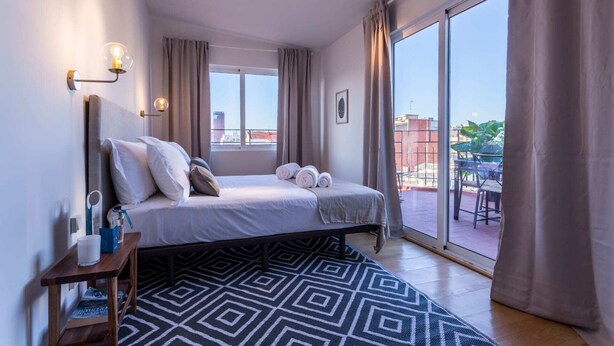 Moderni hotellihuone, jossa on suuri sänky, yöpöytä, ikkuna verhoilla ja näkymä kaupunkiin.
