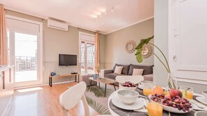 A modern living room with a sofa, a flat-screen TV, and a dining area with a table set for breakfast. - Sweett | Rocafort Atic 3 (Barcelona)