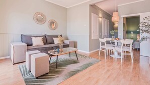 A modern living room with a grey sofa, a coffee table, and a dining area with white chairs and a table. - Sweett | Rocafort Atic 3 (Barcelona)