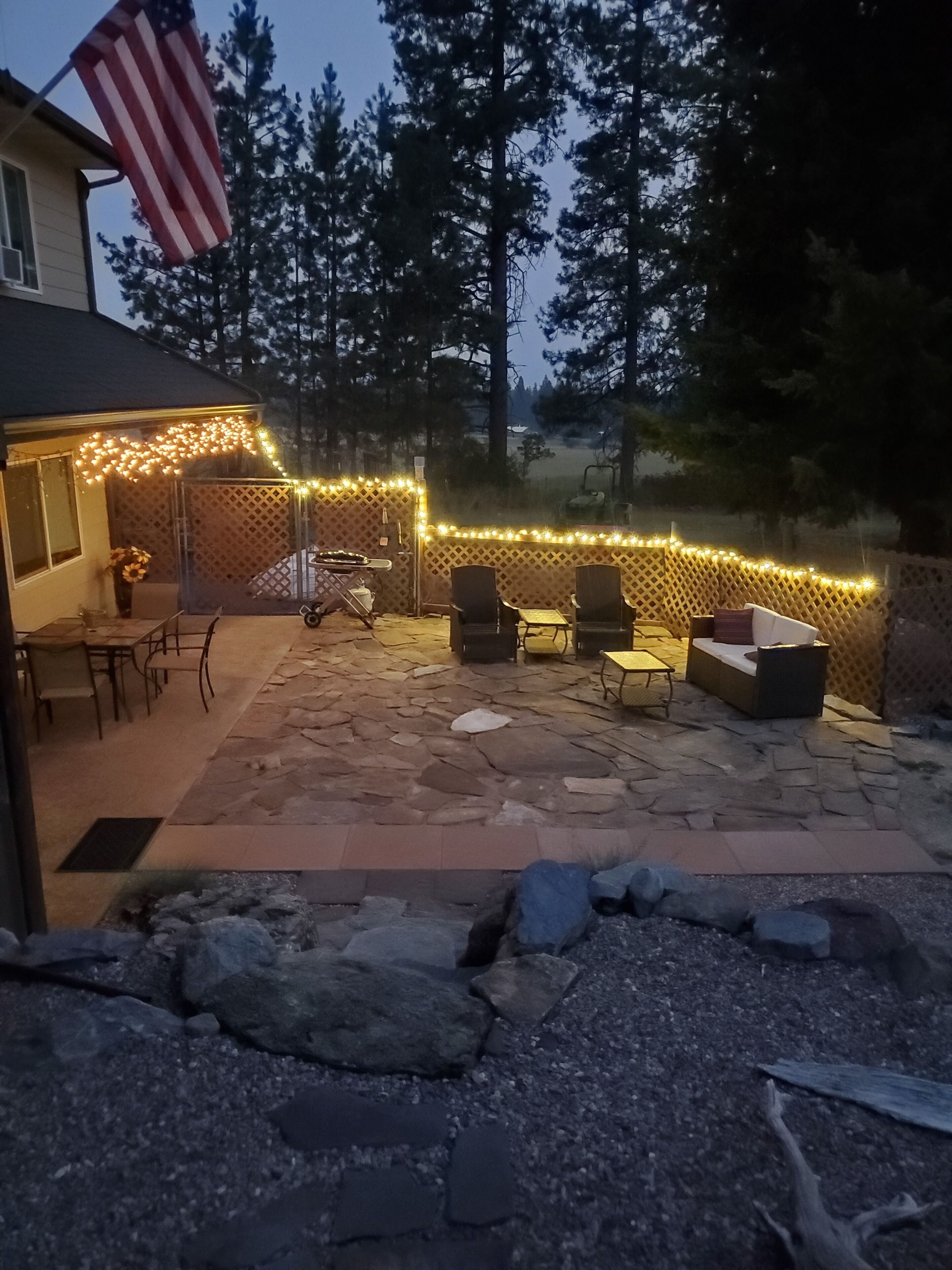 Eine Terrasse mit Steinplatten, Gartenmöbeln und Lichterketten.