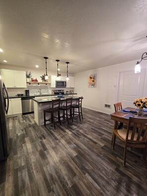 A modern kitchen with a central island, stainless steel appliances, and a dining area with a wooden table and chairs.