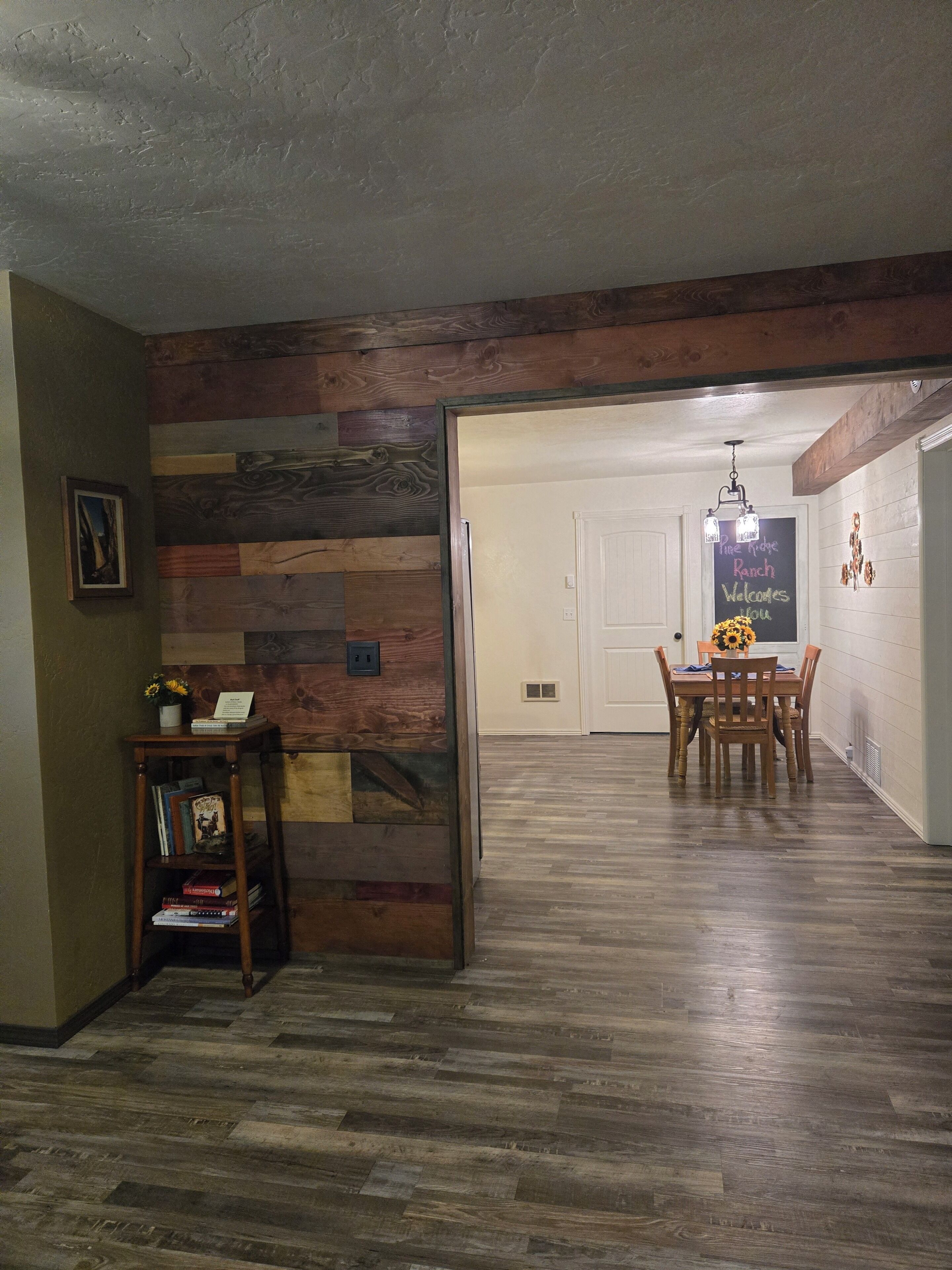 Una habitación con piso de madera, una mesa de comedor con sillas y una puerta que da a otra habitación.