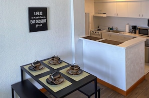 A compact kitchen with a central island, a dining table with four teapots, and a motivational quote on the wall. - Beachfront Studio on Daytona Beach w/ Oceanfront Pool & Free Parking (Daytona Beach)
