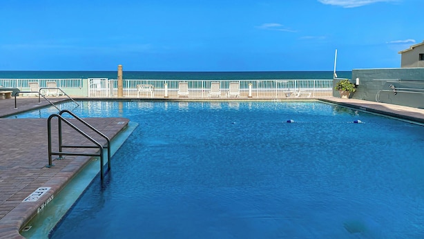 A swimming pool with a view of the ocean, a white fence, and a brick deck. - Beachfront Studio on Daytona Beach w/ Oceanfront Pool & Free Parking (Daytona Beach)