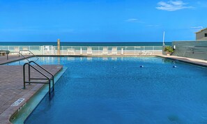 A swimming pool with a view of the ocean, a white fence, and a brick deck.