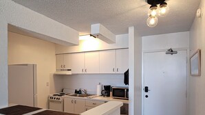 A compact kitchen with white cabinetry, a stove, a microwave, and a sink. There is a door leading to another room. - Beachfront Studio on Daytona Beach w/ Oceanfront Pool & Free Parking (Daytona Beach)