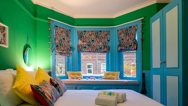 A bedroom with a large bed, a window seat with curtains, and a view of a brick building. - Colourful, Quirky Artist-Owned 3 Bed Next to Cafes - Pass the Keys (Belfast)