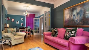 A living room with a pink sofa, a wooden coffee table, and a dining area with a table and chairs. - Colourful, Quirky Artist-Owned 3 Bed Next to Cafes - Pass the Keys (Belfast)