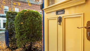 A yellow door with a brass knocker and a nameplate, set against a backdrop of a brick building and a neatly trimmed hedge. - Colourful, Quirky Artist-Owned 3 Bed Next to Cafes - Pass the Keys (Belfast)