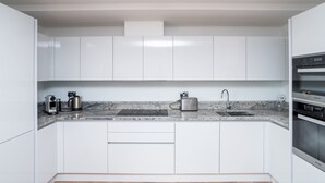 Une cuisine moderne avec des meubles blancs, un plan de travail en marbre, une machine à café, un grille-pain et un four encastré.