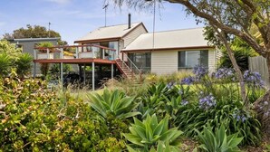 Une maison à deux étages dotée d’un espace extérieur couvert, entourée de différentes plantes et d’arbres.