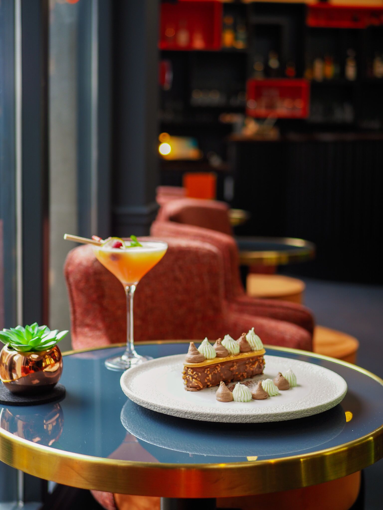 A dessert plate with a chocolate mousse cake and a cocktail on a table in a bar setting.
