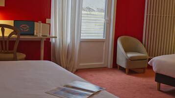 A hotel room with a bed, a desk with a laptop, a chair, and a window with blinds.