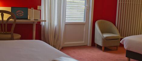 Een hotelkamer met een bed, een bureau met een laptop, een stoel en een raam met jaloezieën.