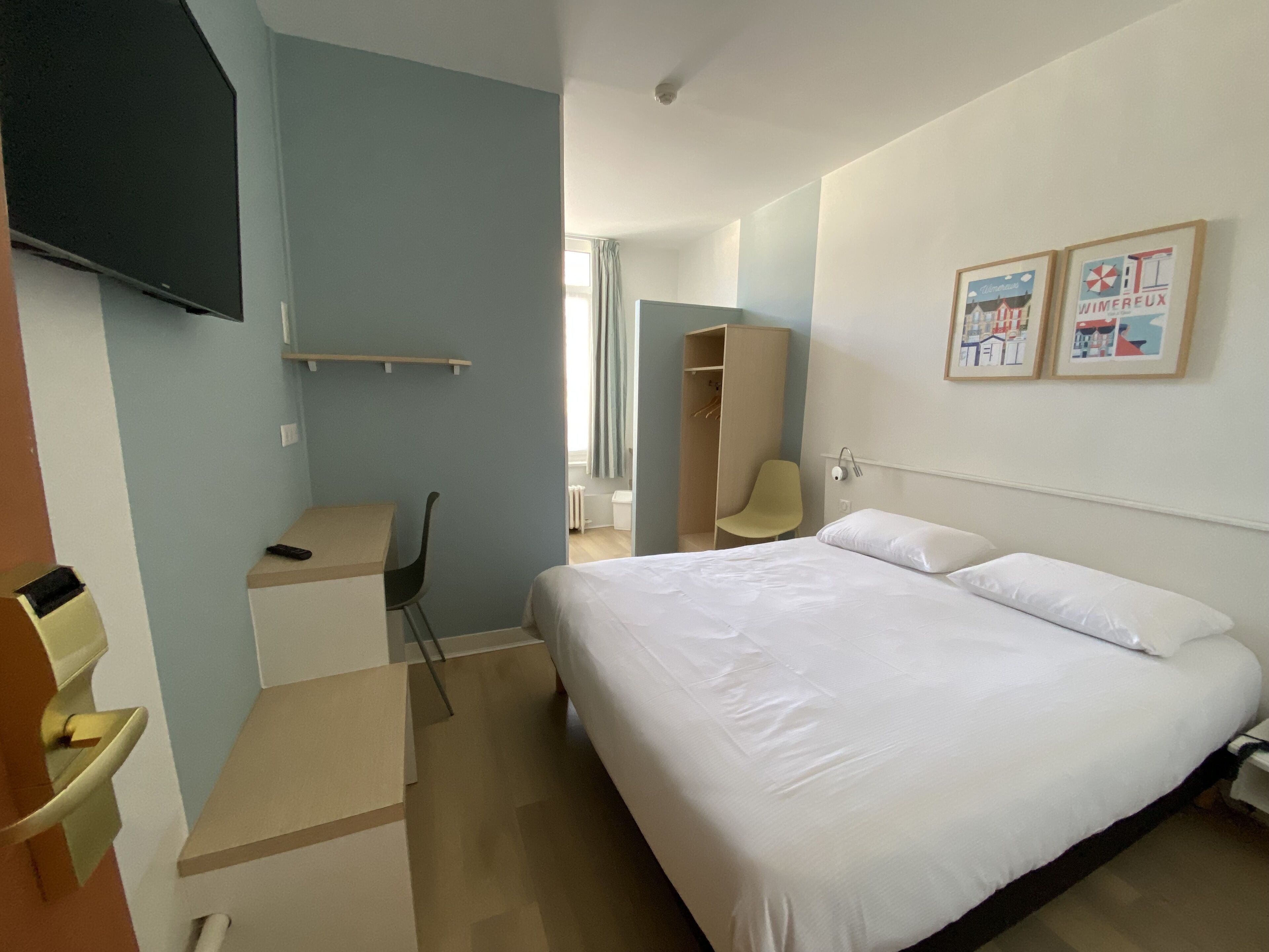 Ein Hotelzimmer mit Bett, Schreibtisch, Stuhl, Kleiderschrank und Fernseher an der Wand.