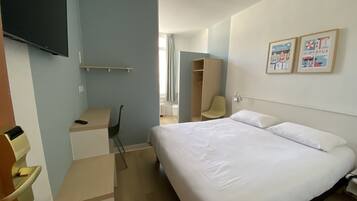 Ein Hotelzimmer mit Bett, Schreibtisch, Stuhl, Kleiderschrank und Fernseher an der Wand.