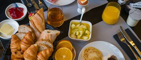 Een ontbijttafel met croissants, fruit, pannenkoeken en diverse soorten beleg.