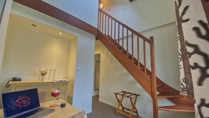 Habitación de hotel con una escalera de madera, un escritorio con una computadora portátil, un jarrón con flores y una bebida.
