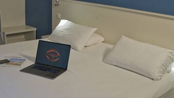 Una cama con ropa blanca, una computadora portátil sobre la cama y una mesita de noche con un teléfono y una tarjeta.