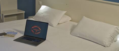 A bed with white bedding, a laptop on the bed, and a bedside table with a phone and a card.