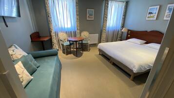 A hotel room with a bed, a sofa, a table with chairs, and a TV.