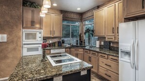 A kitchen with granite countertops, wooden cabinets, a built-in microwave, a stove, and a refrigerator. - Cozy Timbers by Ruidoso Vacation Rentals (Ruidoso)