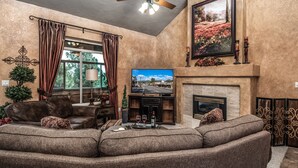 A cozy living room with a sectional sofa, a fireplace, a television, and a ceiling fan. - Cozy Timbers by Ruidoso Vacation Rentals (Ruidoso)