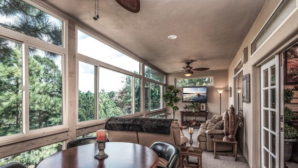 A sunroom with a round wooden table, leather chairs, a sofa, and a television. - Cozy Timbers by Ruidoso Vacation Rentals (Ruidoso)