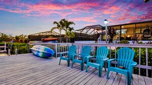 Une terrasse en bois avec des fauteuils Adirondack turquoise et un bateau aux couleurs vives.