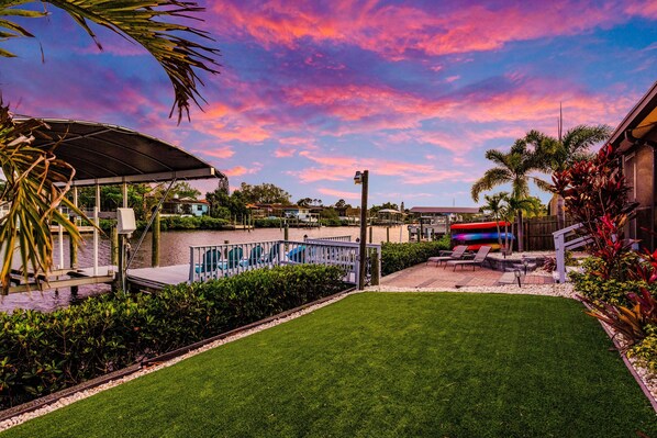 A well-maintained backyard with a swimming pool, a covered patio, and a grassy lawn.